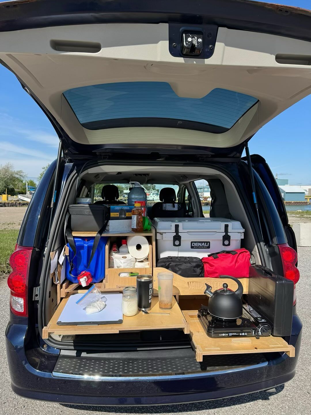An open van trunk displays wooden shelving, cooking equipment, and storage containers.