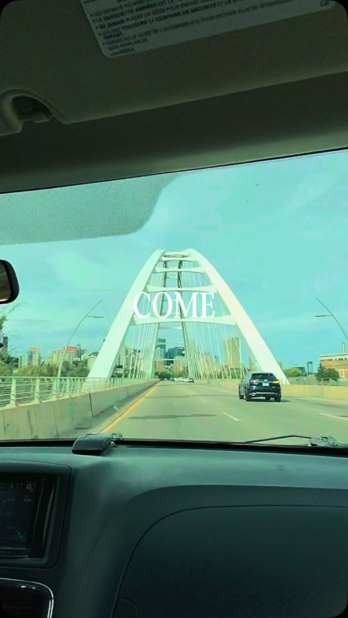 Bridge with white arch and COME text spans across highway ahead.
