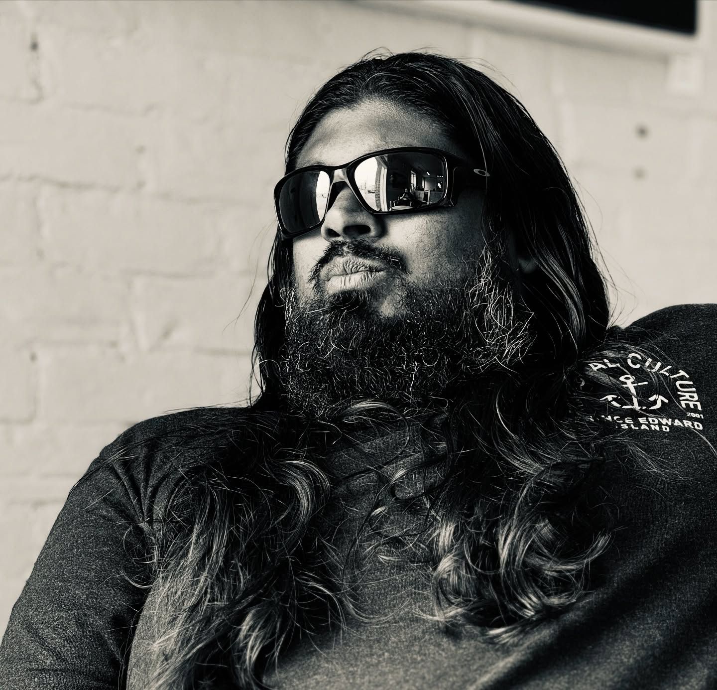 Man with long hair and beard wearing sunglasses in black and white portrait.