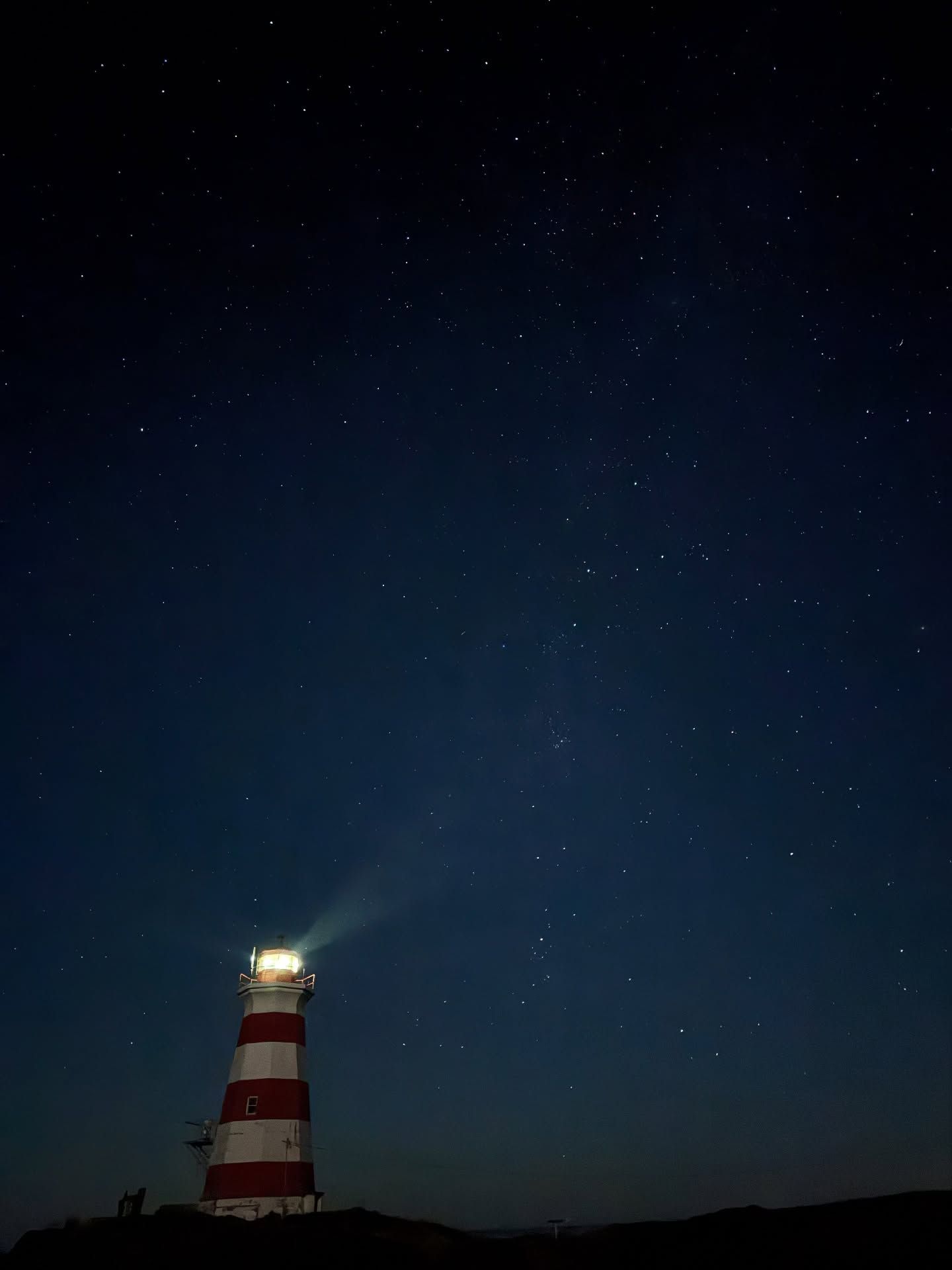 Lit lighthouse with red and white stripes glows against a starry night sky.