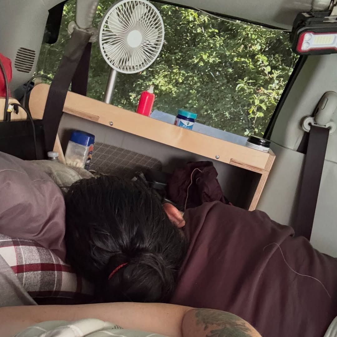 Interior van with portable fan mounted near window and storage shelf.