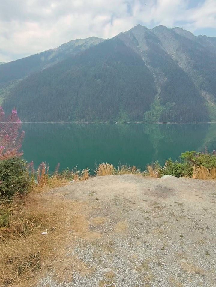 Turquoise mountain lake with rocky shore and forested peaks under blue sky.
