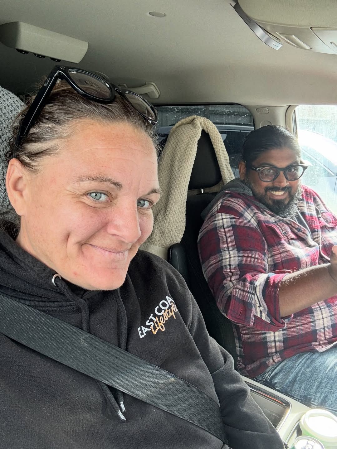 A woman and man smile together in the front seats of a vehicle.