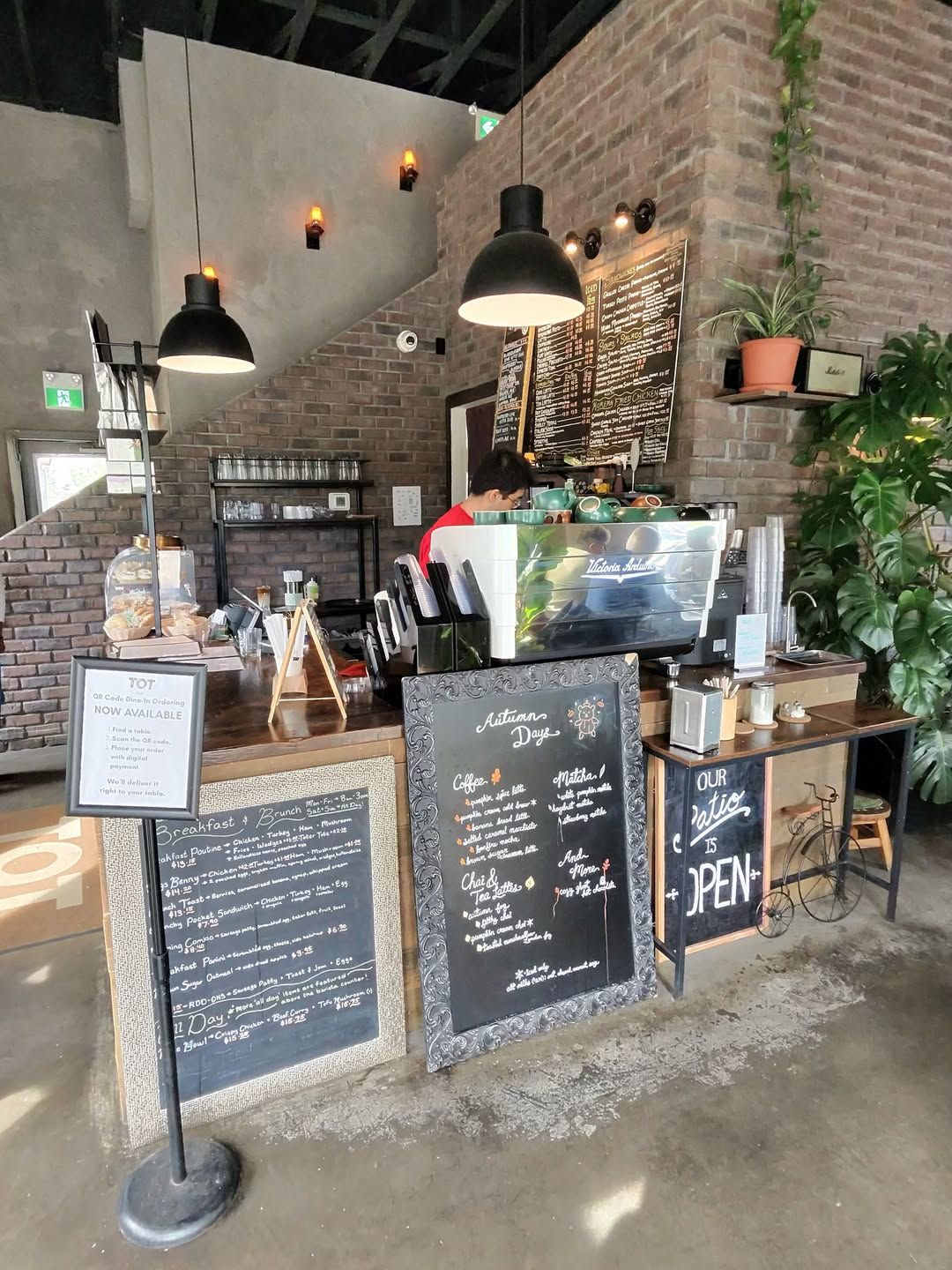 Modern brick coffee shop interior with hanging black lights and barista working.