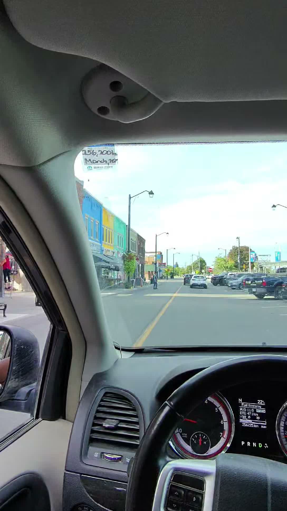 View from van window shows colorful storefront and street parked with cars in daylight.