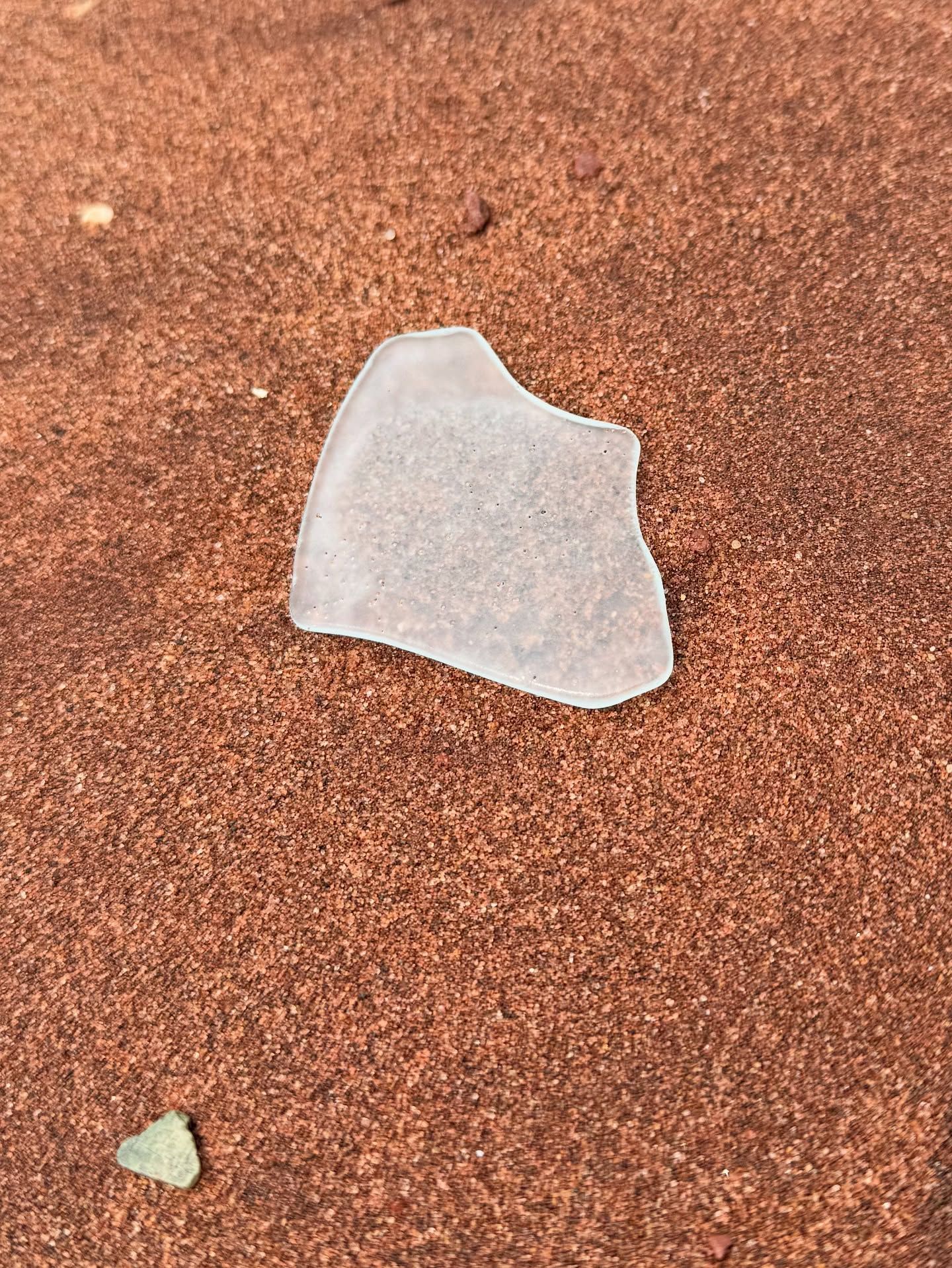 Frosted white sea glass resting on red-brown sand with small stones.