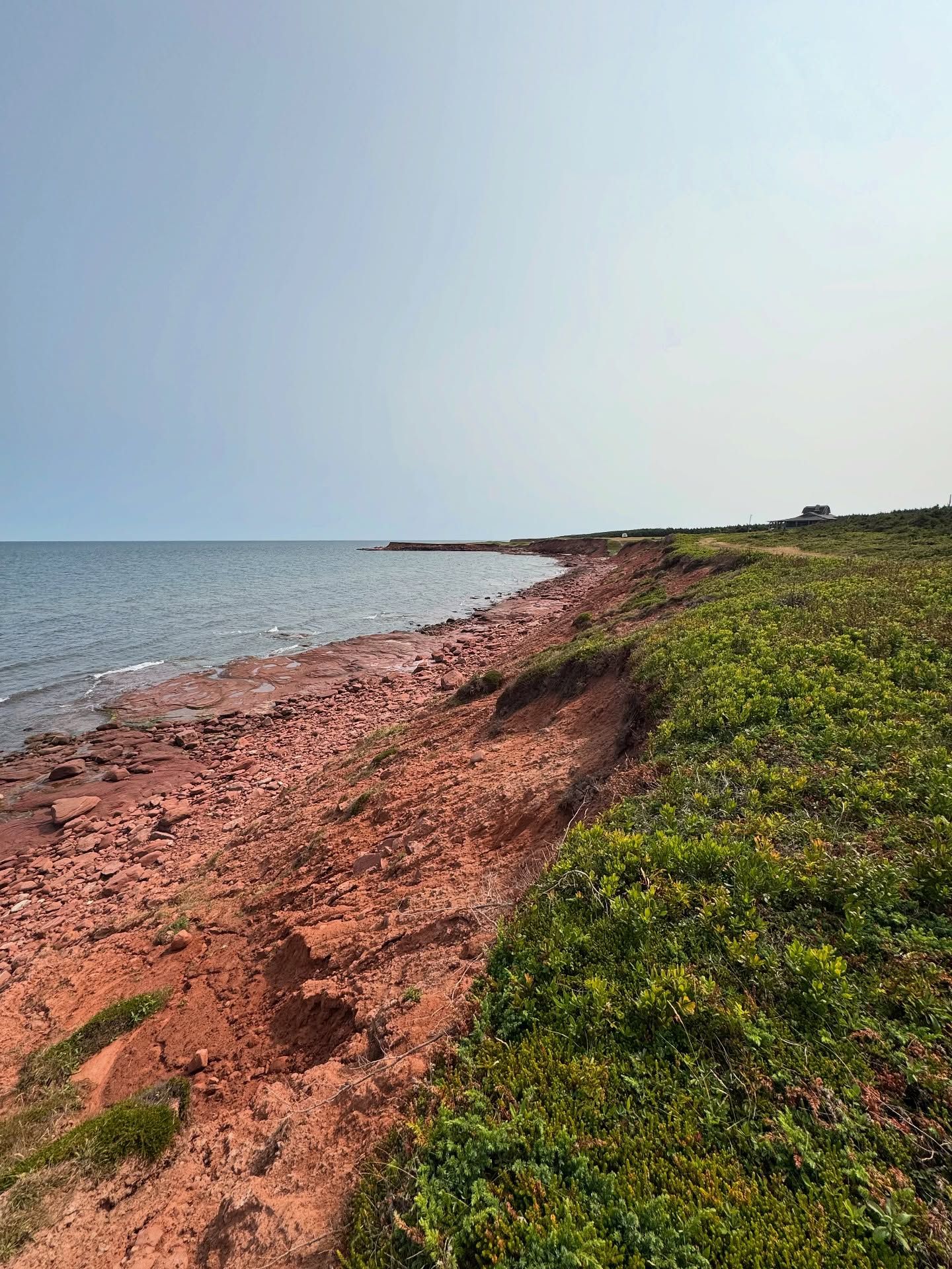 Red sandy coastal landscape with blue water and green vegetation cliff.