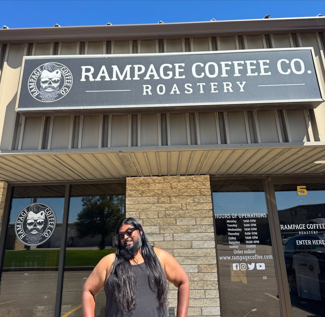 Man with long black hair and beard standing outside Rampage Coffee.
