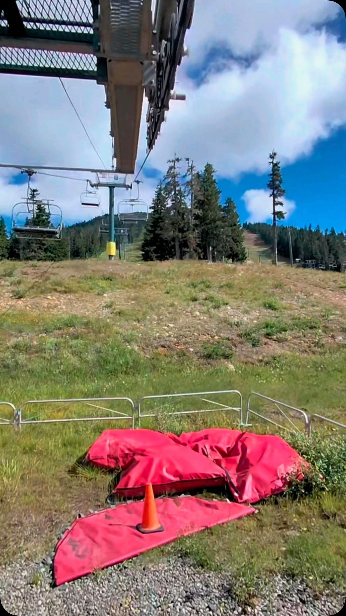 Red parachute on ground beneath ski lift with forested mountains.