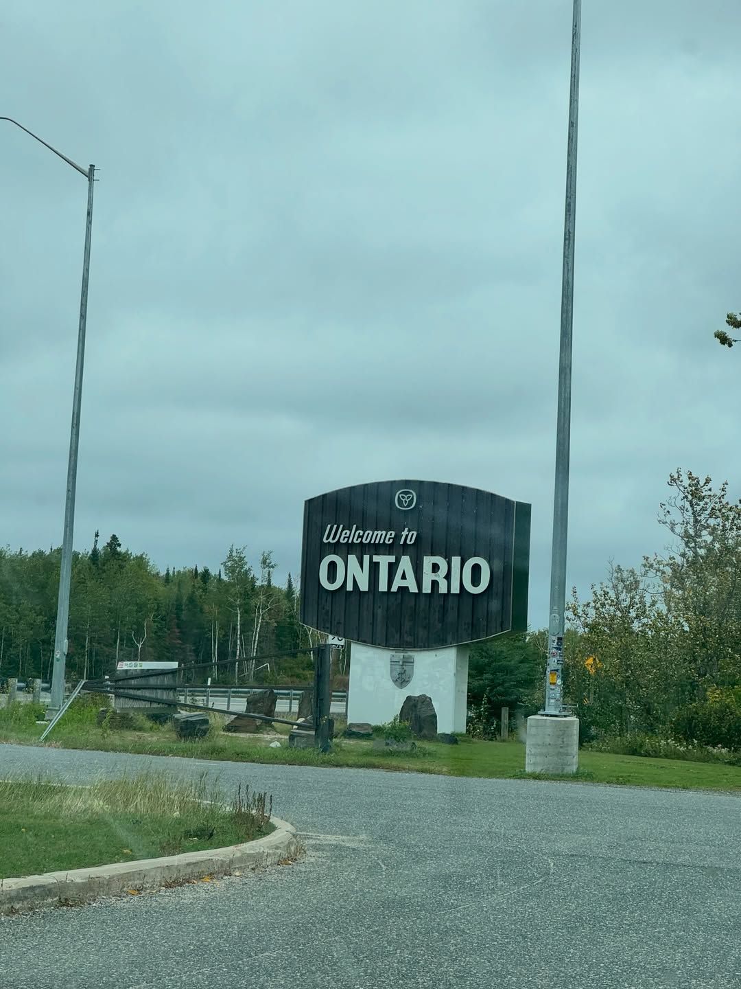 Welcome to Ontario sign on roadside with boreal forest and power lines.