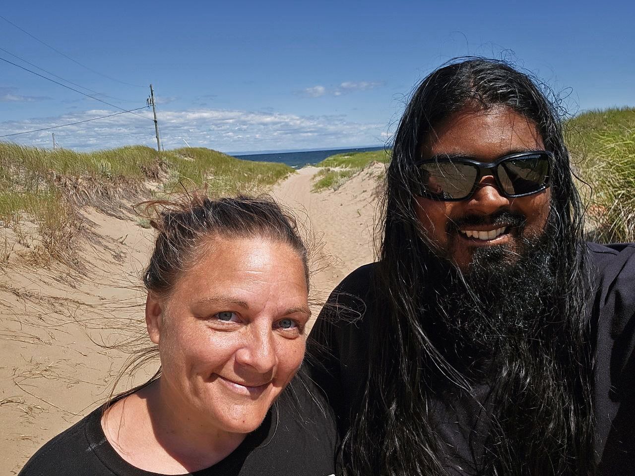 Chey and Mark smiling on sandy beach with ocean and dunes behind.