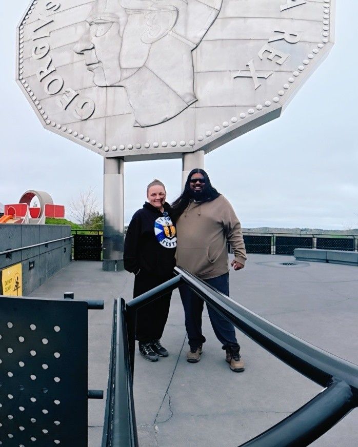 Chey and Mark stand together beneath a massive sculptured coin monument.