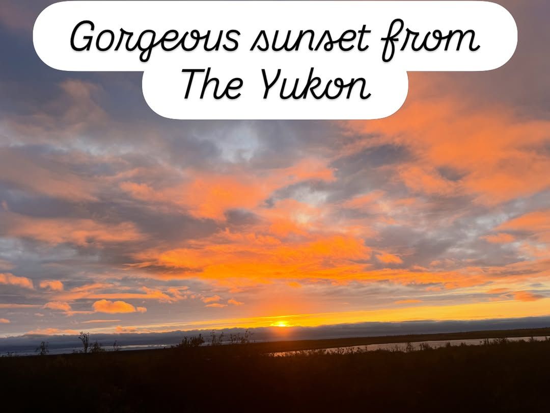 A dramatic orange and yellow sunset illuminates clouds over a distant landscape.