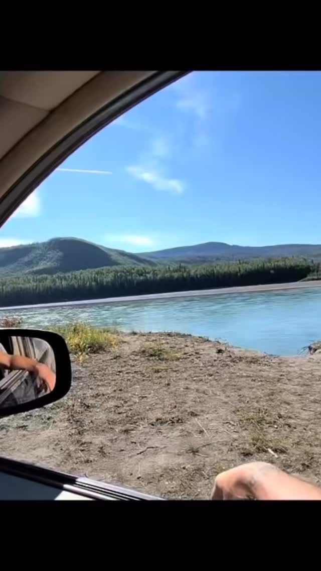 Alpine lake and forested mountain visible through van window in clear weather.