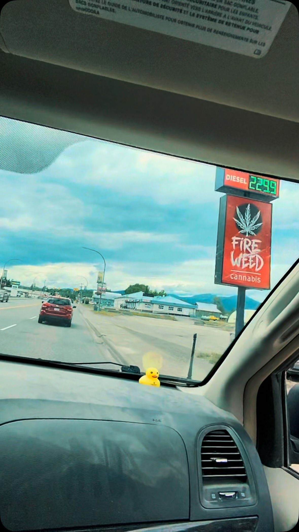 View through van windshield of highway with cannabis shop sign and yellow duck toy.